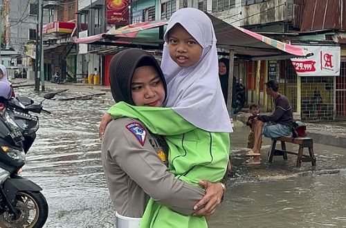 Kasatlantas Polres Dumai saat membantu anak-anak menyeberang akibat banjir.(foto: bambang/halloriau.com)