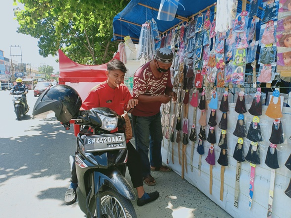 Afrizal saat melayani pembeli masker yang dijualnya di Jalan Bukit Barisan