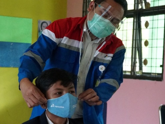 Unit Manager Communication, Relations & CSR RU II Pertamina Brasto Galih Nugroho memasangkan masker kepada salah satu pelajar.
