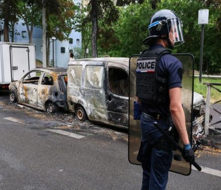 Seorang petugas polisi Prancis berjaga di samping kendaraan yang dibakar pada malam bentrokan antara pengunjuk rasa dan polisi, menyusul kematian seorang remaja berusia 17 tahun yang dibunuh oleh seorang petugas polisi Prancis saat pemberhentian lalu lintas, di Nanterre, pinggiran Paris, Prancis, 1 Juli 2023. REUTERS - Yves Herman
